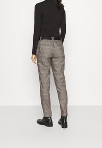 Pantalones de cuadros en tonos de gris y marrón, con un corte slim, dos bolsillos traseros y un cinturón negro. Combinados con una parte superior negra y botas.