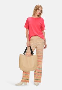 Pink short-sleeve top with fringe, colorful patterned wide-leg pants, and a beige handbag with black straps. Cream block-heeled shoes.