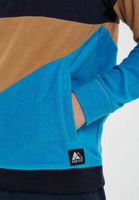 Fleece-Pullover in Marineblau, Braun und Blau mit einer Kängurutasche, geripptem Saum und Logo-Patch. Weiche Textur mit Farbblockdesign.