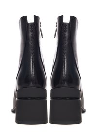 Bottines en cuir noir avec un talon carré, fermeture éclair et détails cousus à l'arrière. Texture lisse avec un design élégant et moderne.