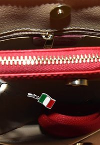 Bordeaux leren handtas interieur met een gouden rits, stoffen voering en een bevestigd zilveren charme met de Italiaanse vlag.
