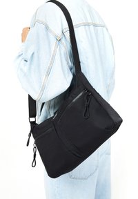 Sac bandoulière noir en tissu durable avec plusieurs poches zippées, une forme triangulaire élégante et une bandoulière adjustable.