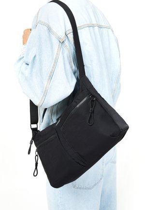 Black crossbody bag made of durable fabric with multiple zippered pockets, a sleek triangular shape, and a adjustable strap.