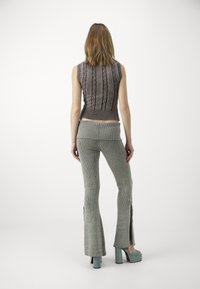 Pletený dvoudílný outfit, který zahrnuje top bez rukávů se vzorovaným steh, a rozevláté kalhoty s žebrovaným vzorem a bočními rozparky; barevné schéma převážně šedé.