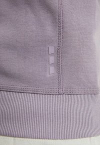 Tela morada texturizada con un dobladillo acanalado. Presenta tres pequeños acentos morados elevados a lo largo de la costura. Diseño liso y elegante.