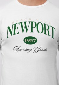 Hvid bomulds T-shirt med grøn tekst: "BEACH CLUB NEWPORT 1957" og "Sporting Goods" i kursiv, med en glat overflade og rund halsudskæring.