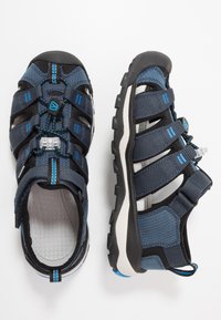 Sandálias desportivas para homem, parte superior em malha azul escuro e preta com tiras elásticas, sola em borracha e faixa de calcanhar ajustável. Interior texturizado.