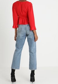 Blouse rouge à manches longues avec un ourlet à volants, associée à un jean taille haute bleu clair à jambes droites et des bottines noires.