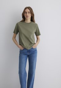 Olive green cotton t-shirt with a round neckline and short sleeves, paired with light blue denim jeans featuring a fitted waist and straight legs.