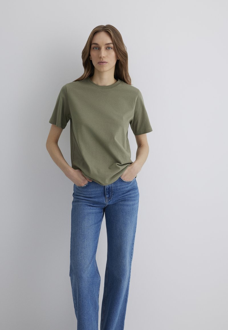 Olive green cotton t-shirt with a round neckline and short sleeves, paired with light blue denim jeans featuring a fitted waist and straight legs.