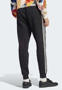 Svarta joggers med vita sidostråk, design med smal ben, mjukt tyg, synliga sömmar, och parat med svarta skor och vita strumpor.