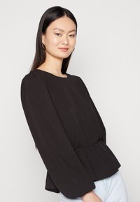 Blusa peplum preta com mangas longas e um tecido texturizado. Apresenta um decote redondo e uma cintura franzida para dar forma e ajuste.