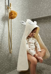 Hooded towel in cream with grey accents, featuring animal ears. Soft texture, suitable for children. Set against a gray tiled background.