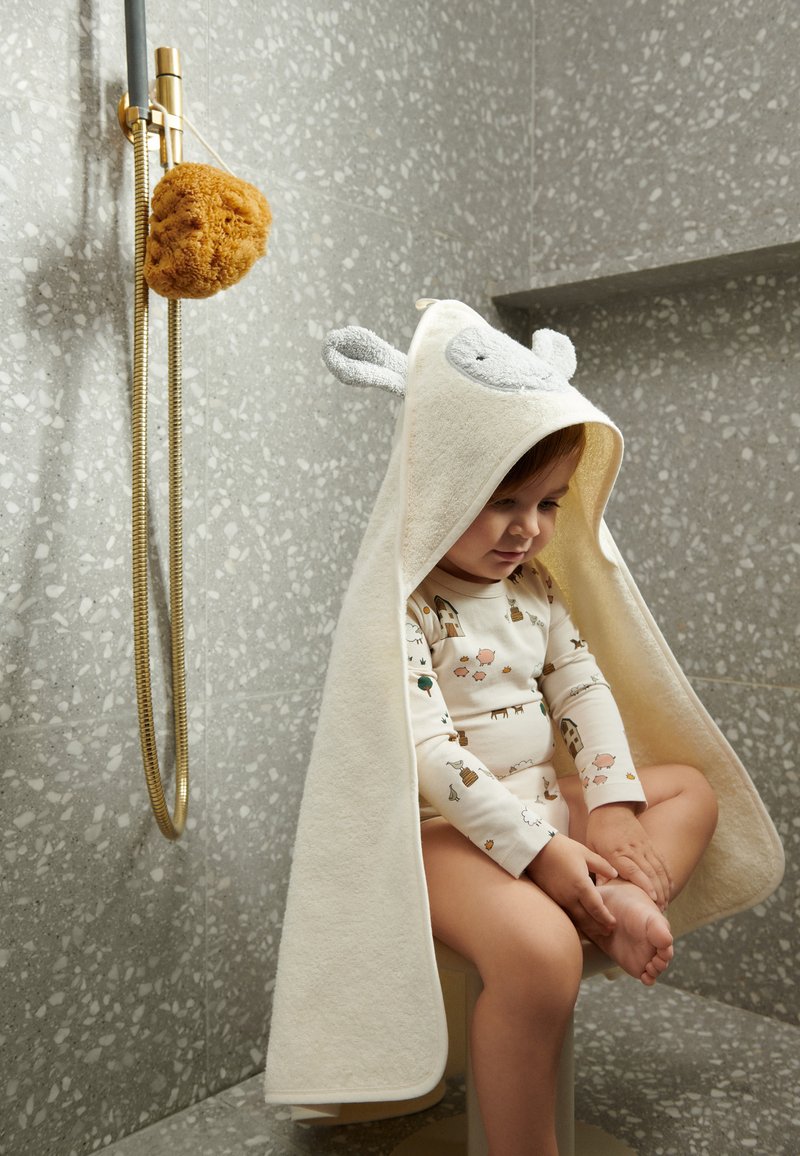 Hooded towel in cream with grey accents, featuring animal ears. Soft texture, suitable for children. Set against a gray tiled background.