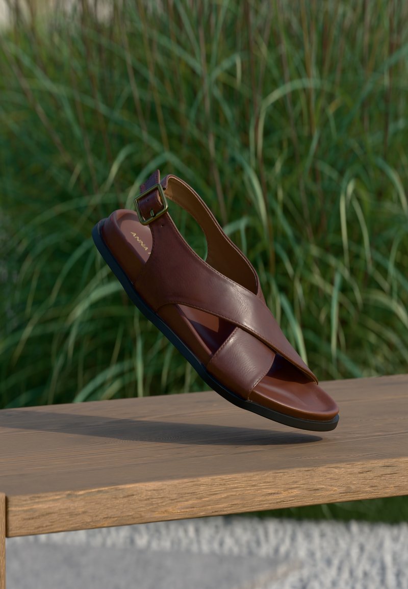 Καφέ δερμάτινο σανδάλι με σχεδιασμό σταυρωτών λουριών, λεπτομέρεια αγκράφας στον αστράγαλο και υφασμένη μαύρη καουτσούκ σόλα.