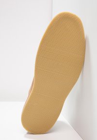 Sole di scarpa marrone con una superficie in gomma testurizzata, caratterizzata da un motivo ondulato per una maggiore aderenza. Il bordo è leggermente arrotondato e liscio.