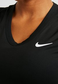 Top atlético negro con diseño de cuello en V, cuello acanalado y un logo de Nike en blanco en el lado izquierdo. Hecho de una tela texturizada.