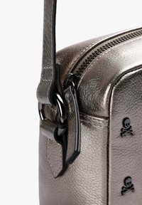 Bolso de mano metálico plateado con superficie texturizada, cierre de cremallera y acentos de calavera negra. Incluye una correa desmontable y herrajes resistentes.