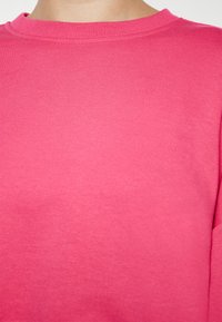 Felpa in cotone rosa con collo rotondo, texture morbida e colletto a coste. Presenta un colore uniforme senza motivi o grafiche visibili.