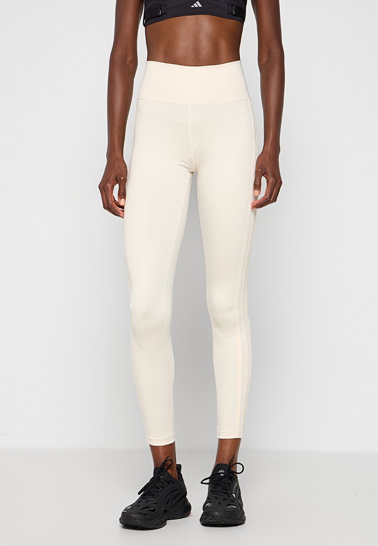 Leggings a vita alta di colore crema con una texture liscia e cuciture laterali. Abbinati a sneaker sportive nere per un look sportivo.