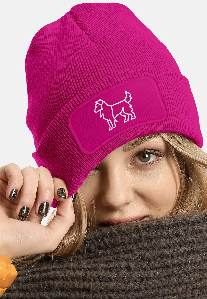 Bright pink knit beanie with a ribbed texture, featuring a rectangular patch with a white dog graphic. Subtle crown seam detail visible.