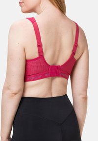 Różowy sportowy biustonosz z teksturowanym, siateczkowym tyłem, regulowanymi ramiączkami i zapięciem na trzy haftki. W zestawie z czarnymi legginsami z wysokim stanem.