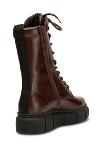 Botte haute en cuir marron foncé avec fermeture éclair latérale, semelle épaisse noire, languette de talon en tissu noir et lacets sur le devant.