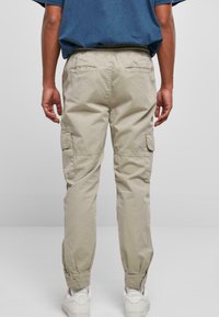 Beige cargobukser med elastisk liv, to sidelommer og oppbrettede kanter, laget av lett stoff, vist fra baksiden.