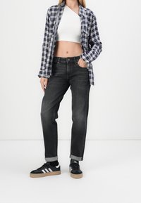 Jeans neri con una vestibilità ampia, abbinati a un top corto bianco e a una camicia oversize a scacchi blu navy e bianca. Sneakers nere con strisce bianche.