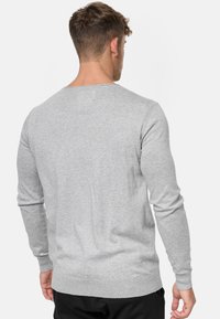 Suéter gris con cuello redondo, mangas largas, puños y dobladillo de canalé, hecho de un tejido de punto suave y texturizado. Se muestra la vista posterior.