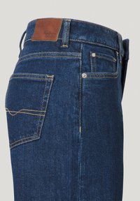 Tmavě modré džíny z denimu s hladkým povrchem, hnědá kožená nášivka na pásku, žluté prošívání a jeden detail zadní kapsy.