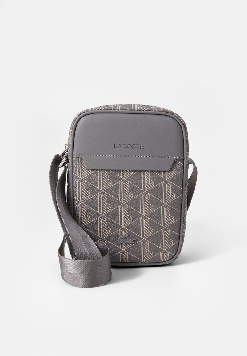 Gray geometric-patterned crossbody bag with a smooth fabric finish, adjustable strap, and a top flap. Features "LACOSTE" embossed logo.