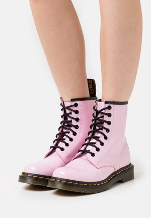 Růžové lakované kotníkové boty s černými tkaničkami, černými detaily, žlutým prošíváním na podešvi a poutkem na zadní straně.