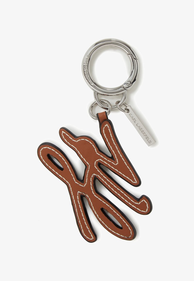 Brun lädernyckelring med en stiliserad logotyp. Den har vit söm och en silvermetallring med en liten hängande etikett.