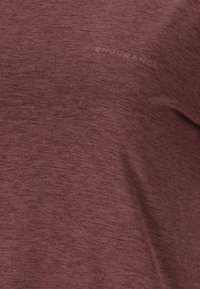 Mörkröd idrottströja med en strukturerad, melerad yta. Har ordet "ENDURANCE" subtilt tryckt nära halslinningen.