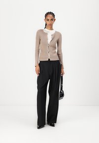Beige ribbed cardigan with button front, worn over a white top, paired with high-waisted black trousers and a small black handbag.