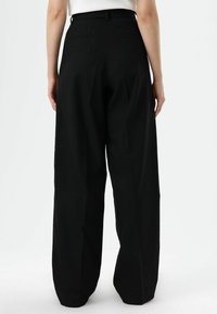 Schwarze, weit geschnittene Hosen mit hoher Taille, ausgestattet mit Gesäßtaschen und einer glatten Stoffstruktur, maßgeschneidert für eine lockere Passform.