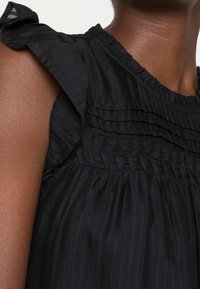 Top nero con texture, caratterizzato da un collo arricciato, righe verticali e vita arricciata. I dettagli includono pieghe orizzontali vicino alle spalle.
