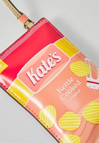 Rote und gelbe Verpackung mit "Kate's Kettle Cooked Original" und Illustrationen von gewellten Kartoffelchips sowie einem goldenen Band. Glatte, glänzende Oberfläche.