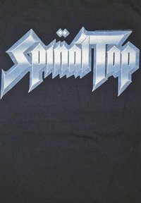 Musta t-paita, jossa on suurikokoinen metallinhohtoinen hopeinen teksti "Spinal Tap" kulmikkaassa, tyylitellyssä fontissa. Silkkinen kankaan pinta.