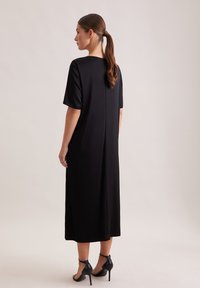 Czarna sukienka midi z krótkimi rękawami, o prostym kroju, z rozcięciem z tyłu. Gładka faktura, wykonana z lekkiego materiału, zestawiona z sandałkami na cienkich paseczkach.