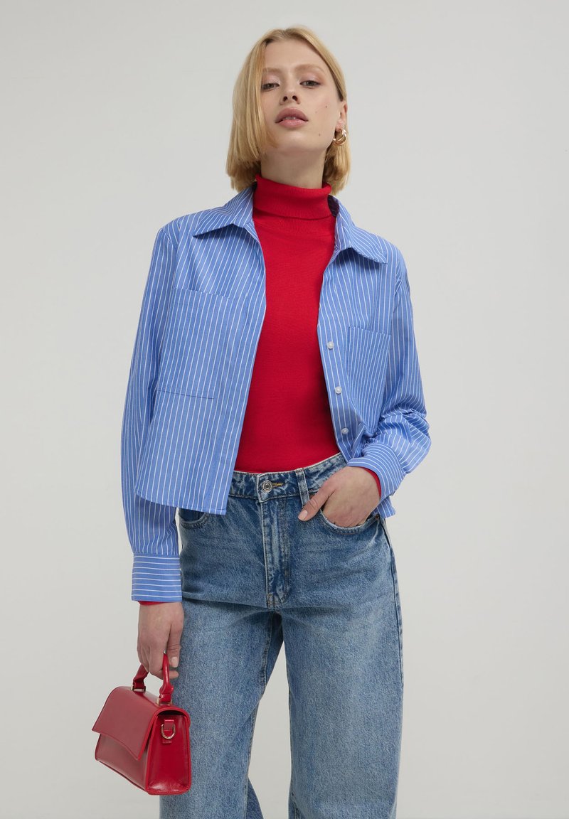 Blauschen gestreiften Hemd mit Knopfleiste, einem roten Rollkragenpullover darunter, hochtaillierte Jeans und einer kleinen roten Handtasche.