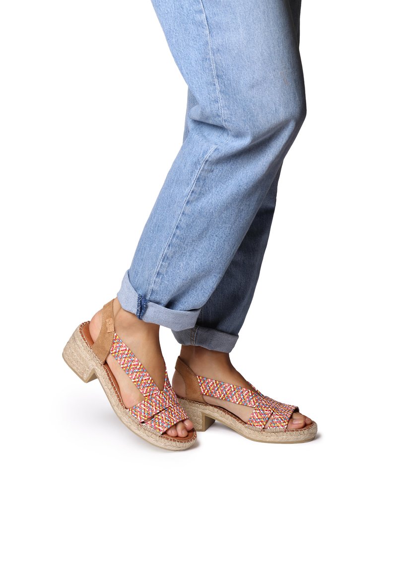 Brown and multicolor woven sandals with a block heel, featuring open straps and a textured sole, paired with rolled blue denim jeans.