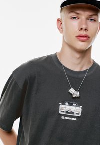 Ung person iført en mørk t-shirt med et billede af en hvid Honda NSX bil og et sølv boksehåndsko som halskæde.