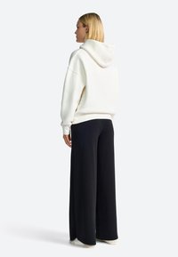 Weißer, übergroßer Hoodie mit Kapuze, kombiniert mit schwarzen, weit geschnittenen Hosen, von hinten gesehen, zeigt den weichen Stoff und den lässigen Schnitt.