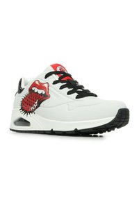 Scarpa atletica bianca con accenti neri, caratterizzata da una grafica rossa e nera di labbra e spuntoni. Design aerodinamico con sovrapposizioni testurizzate e lacci neri.