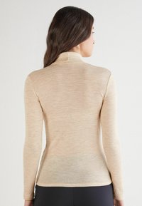 Beige Langarmrollkragenoberteil aus strukturiertem Stoff, mit einer enganliegenden Passform und hohem Kragen, glatter Oberfläche und minimalen Nähten.