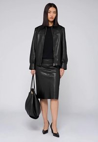 Černá kožená bunda na zip, černý top, kožená sukně s vysokým pasem a černá kabelka; modelka má na sobě černé špičaté podpatky.