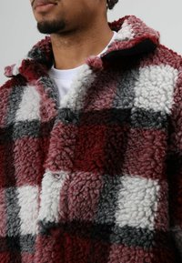 Rood, grijs en wit geruit fleecejack met een zachte, gestructureerde afwerking. Voorzien van een kraag en knoopdetail, met een comfortabel ontwerp.