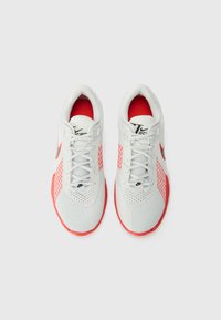 White athletic shoes with red accents, featuring a textured mesh upper, synthetic overlays, and a cushioned sole. Laces and branding visible.